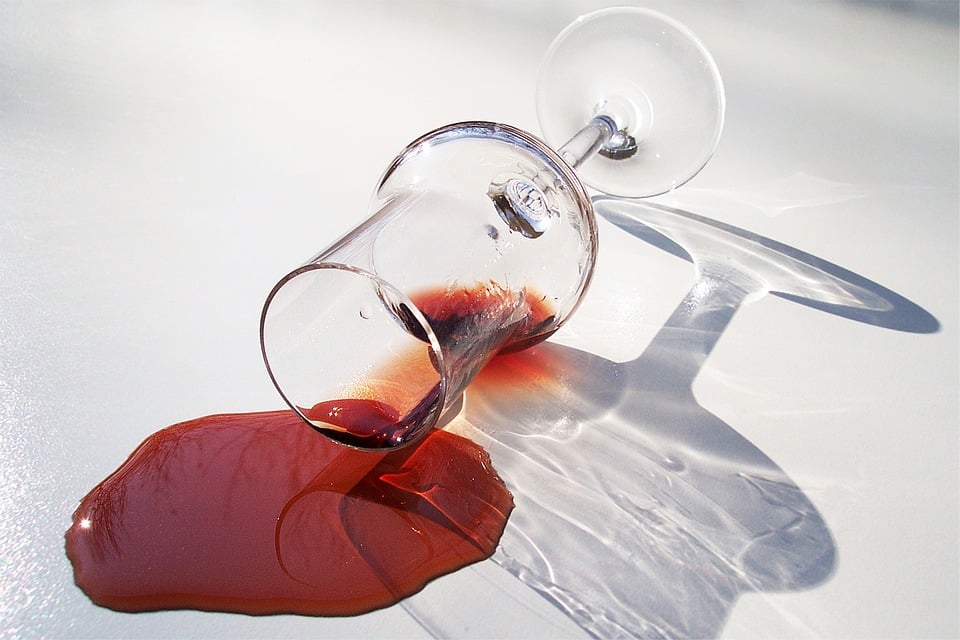 Glass of wine spilled on white background.