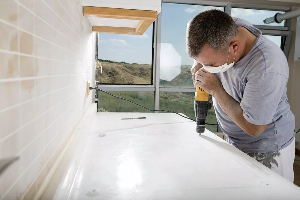 Man using a drill to make a hole into a granite countertop.